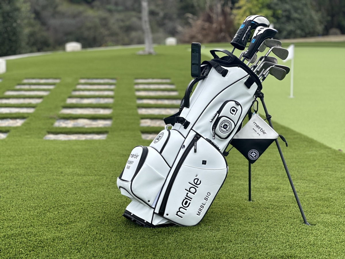 The white Marble bag standing on a putting green, clubs in, towel folded beside it