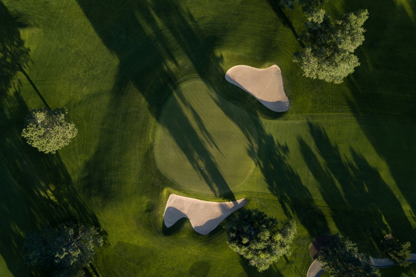 Aerial view of a green and sand bunkers crossed by long tree shadows