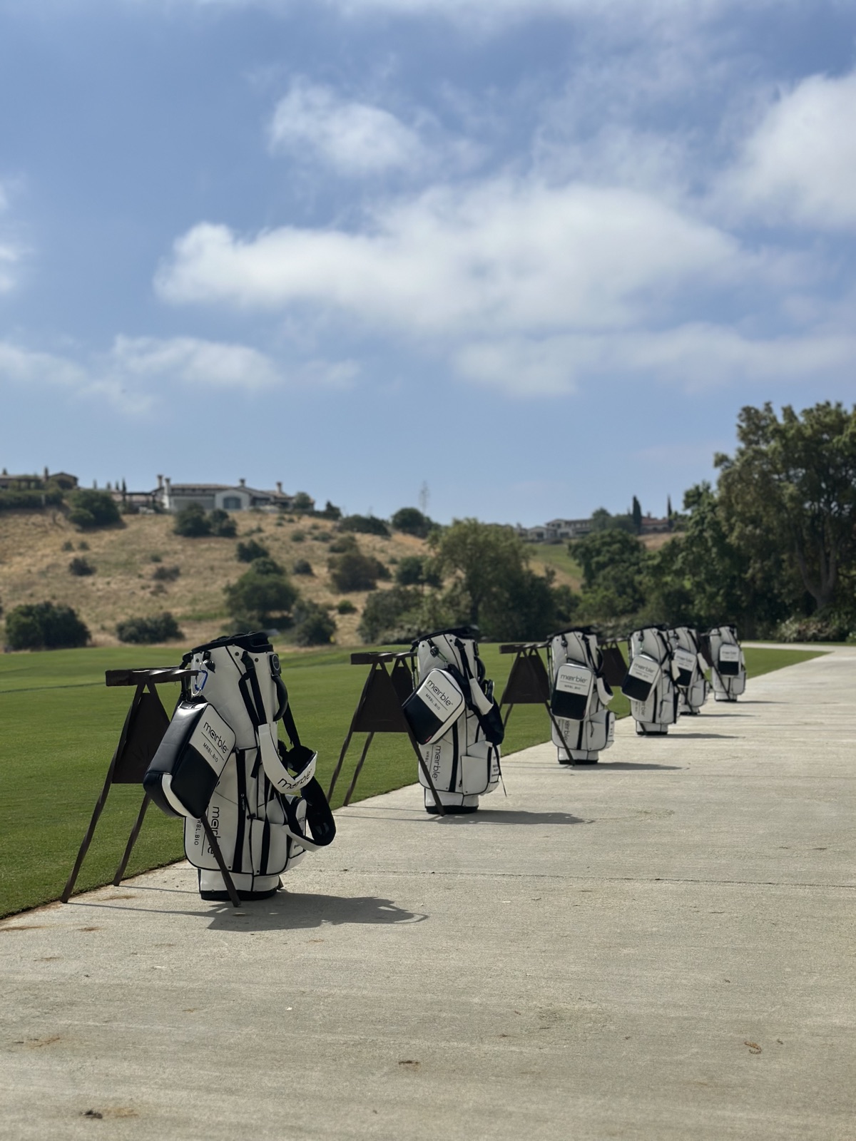 A row of white Marble golf bags lined along a driving range path under a big blue sky